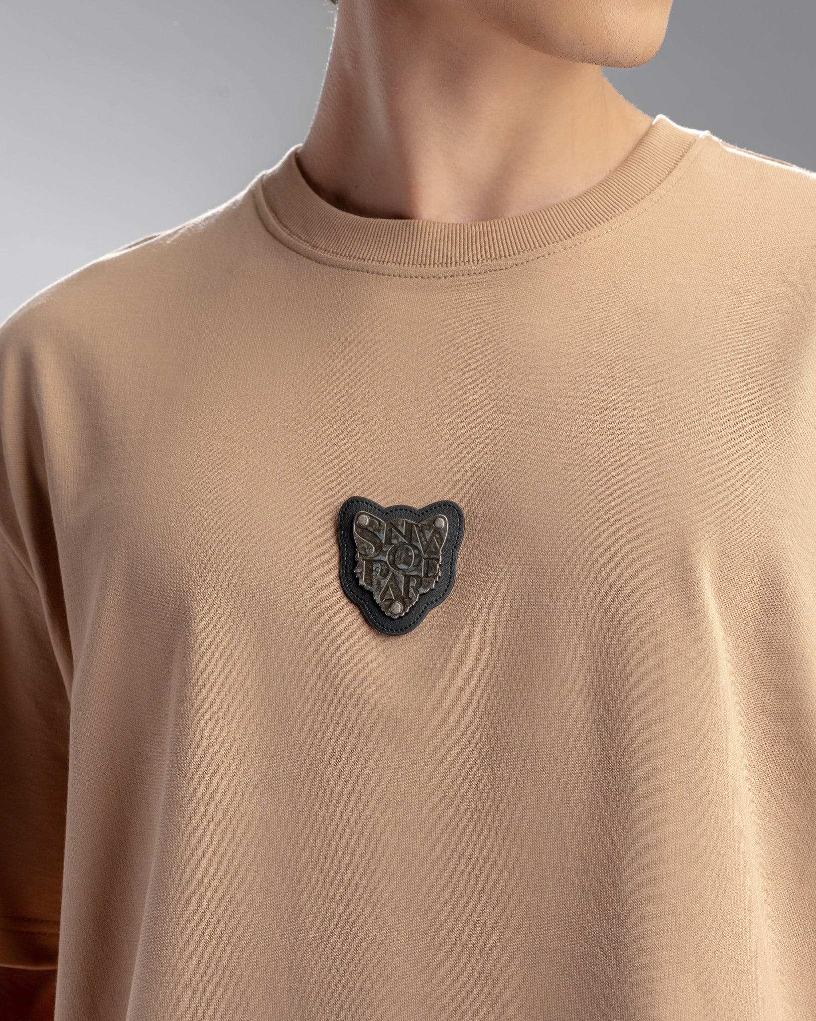 Snowpard Metal Badge Relaxed Tee Sand — back view, structured Snowpard emblem patch