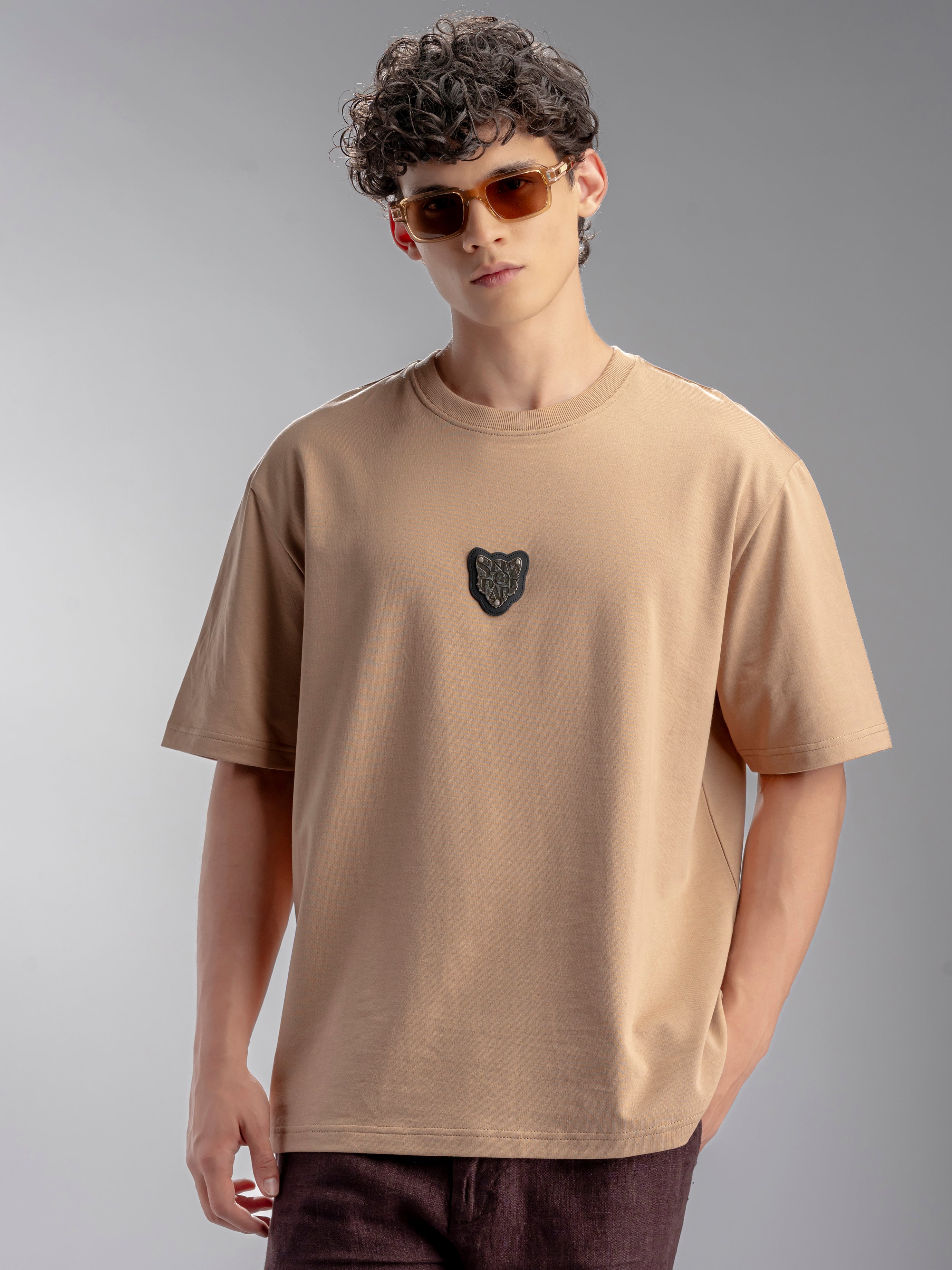 Man wearing a beige t-shirt with a metal logo