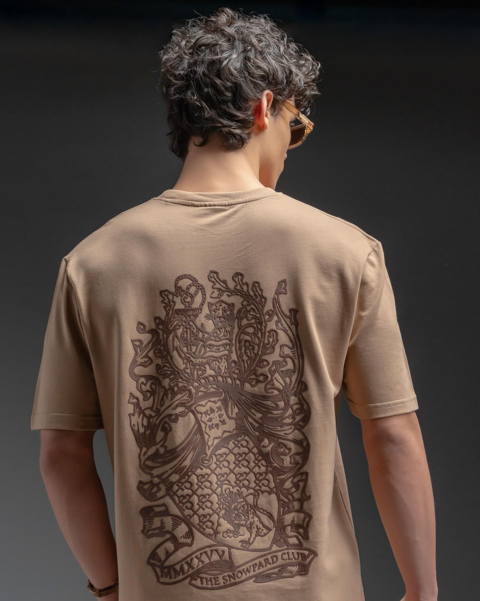 Snowpard Club Crest Relaxed Tee Desert Tan — chest insignia detail, crest emblem close-up