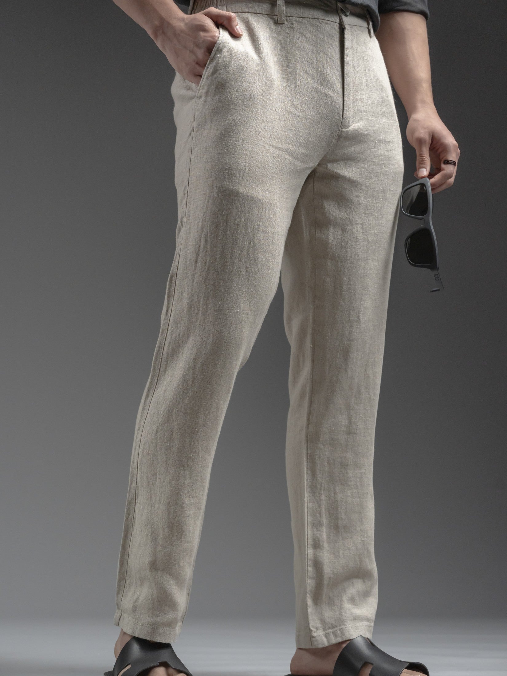 Beige linen pants worn by a person on a gray background