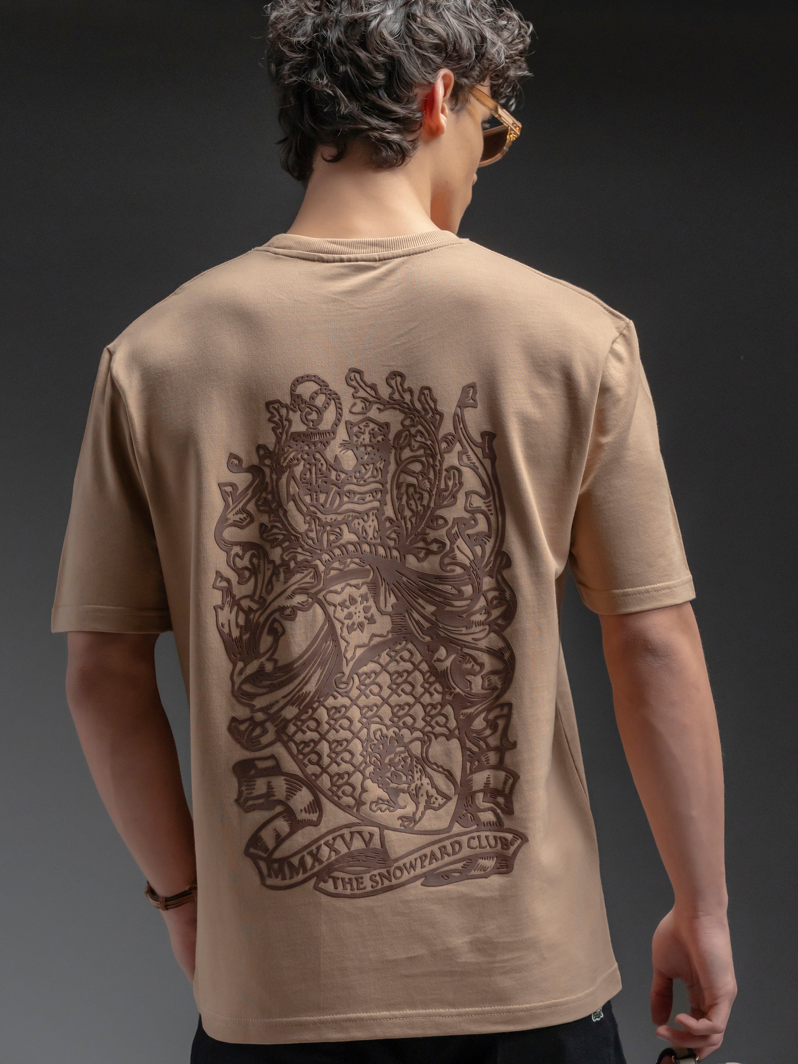 Man wearing a beige t-shirt with a detailed emblem on the back 